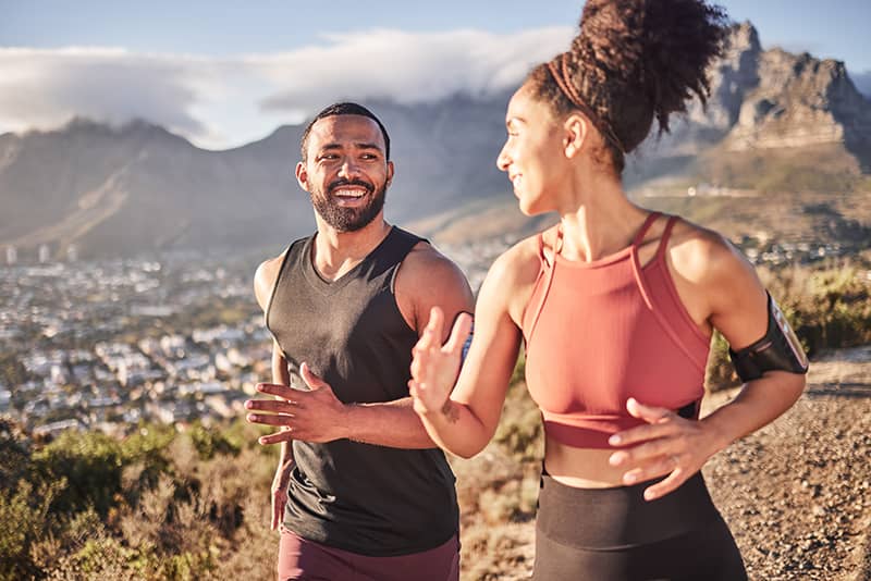 A man and woman in athletic wear run together on a mountain trail.