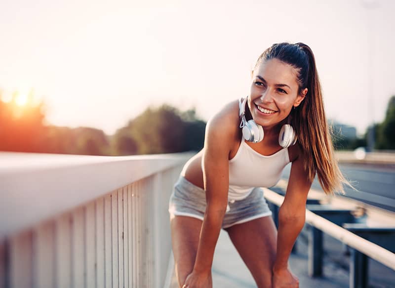 A woman in athletic wear smiles as she rests on a railing after working out.