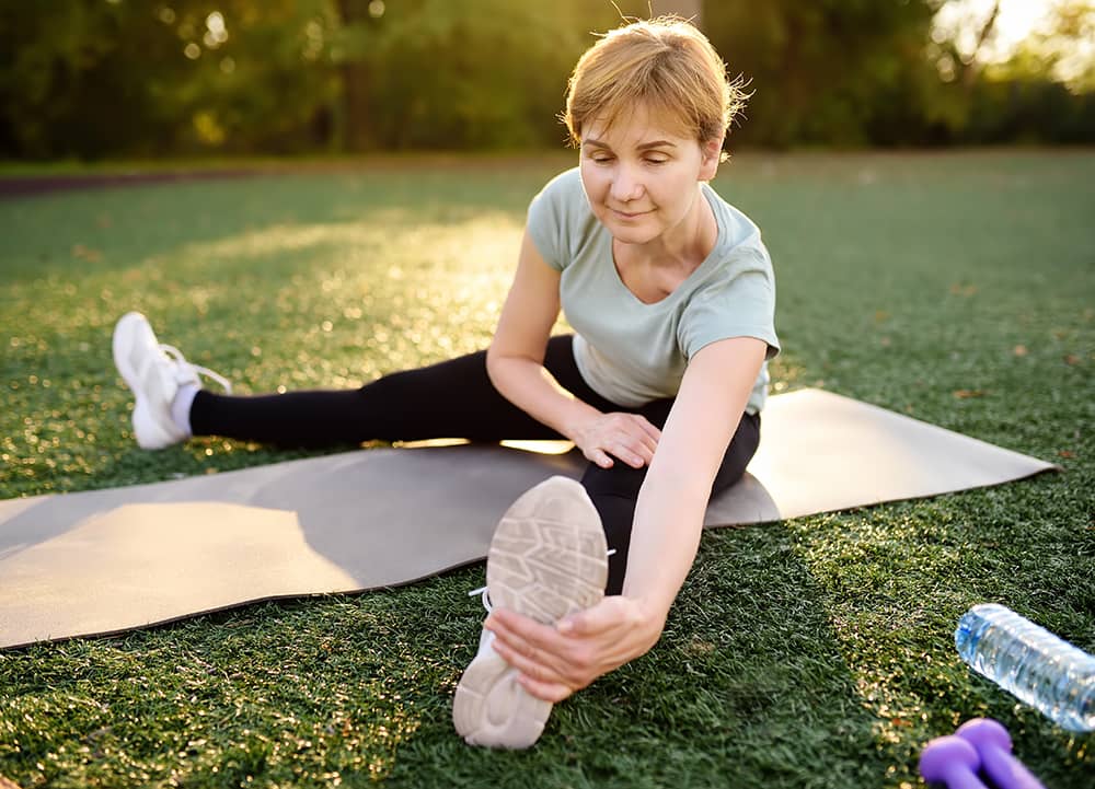 A woman in athletic wear stretches on a yoga mat in a park.