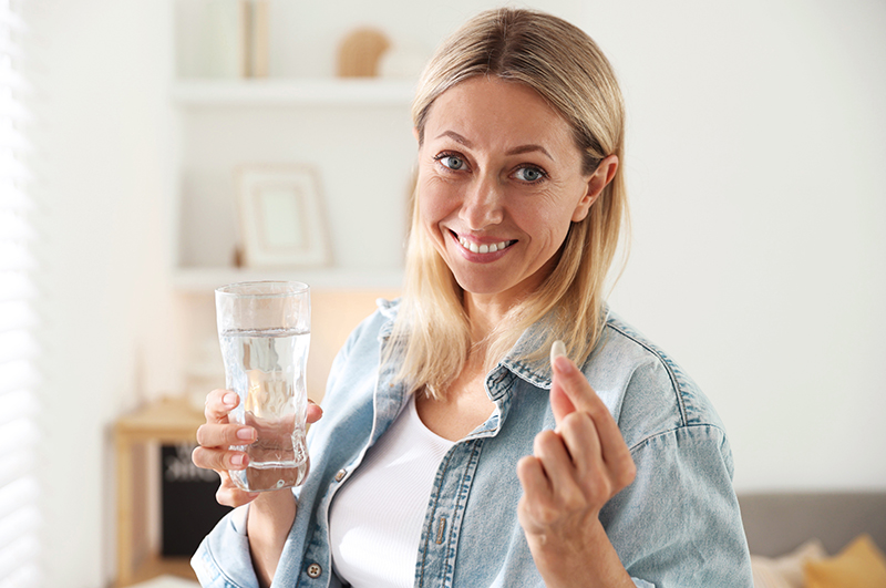 Happy woman with pill and glass of water at home