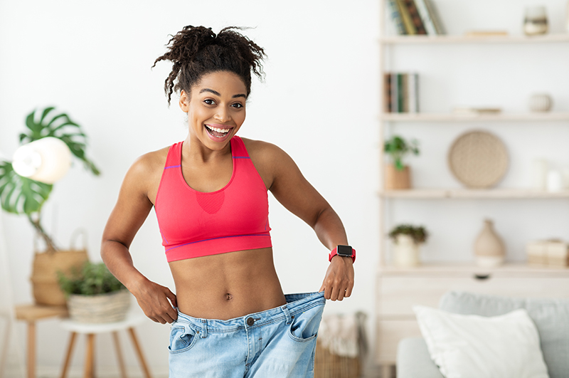 Happy woman showing off weight loss, holding up loose jeans.